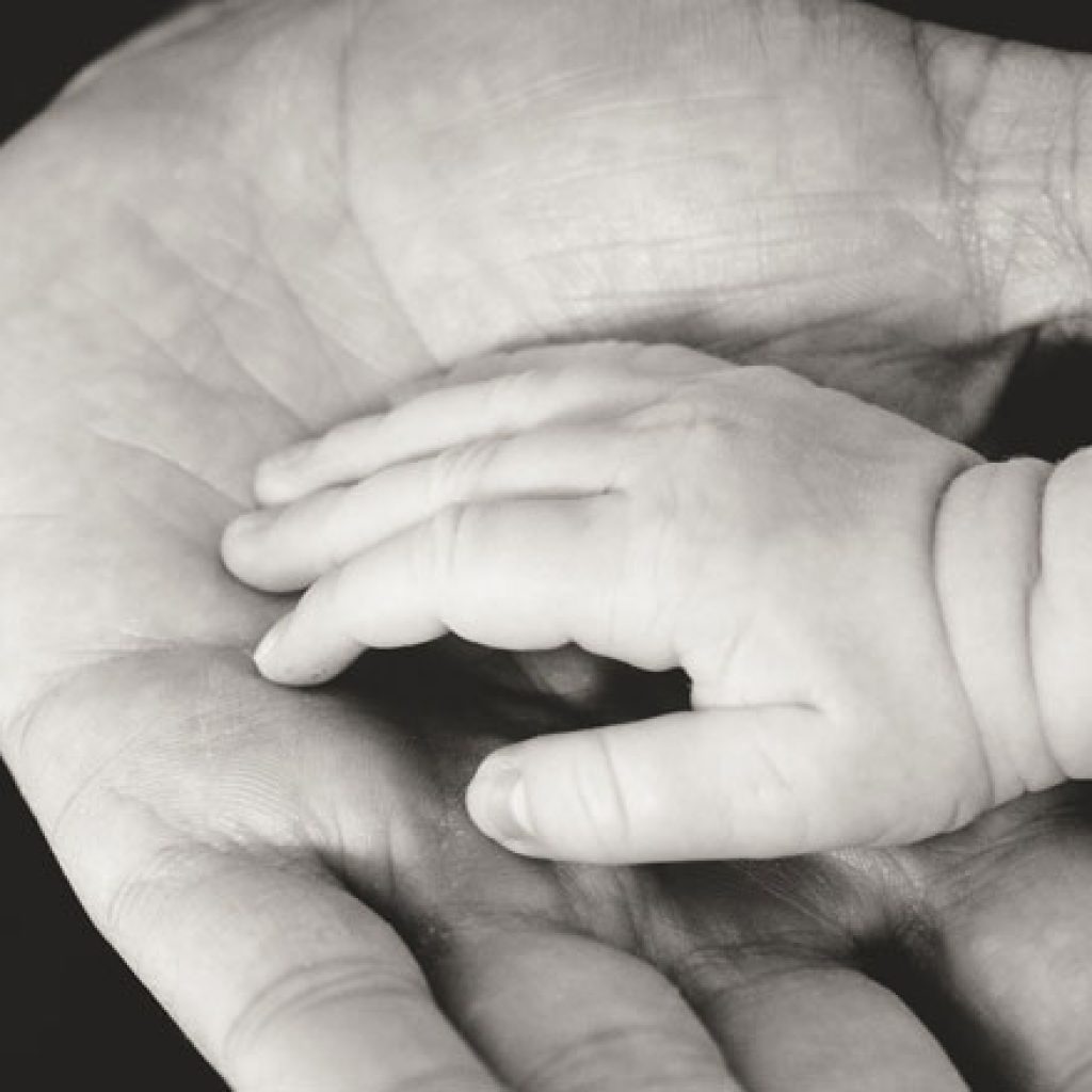 Mano de un bebé sobre la palma de la mano de su papá.
