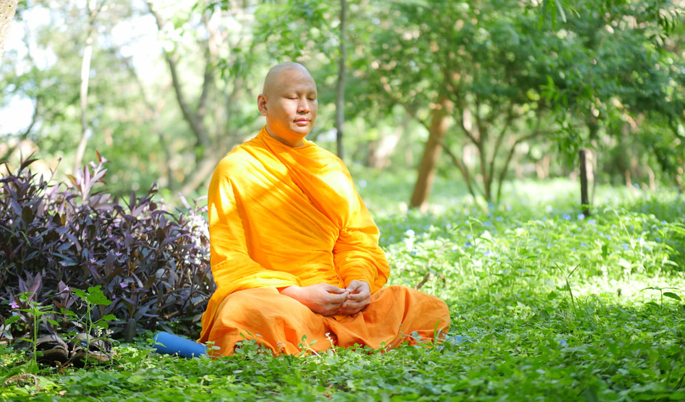 Luang Phi Pasura meditando en un parque verde.